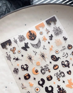 Macro detail of Halloween nail stickers with ghost and spider web designs on a ceramic tray