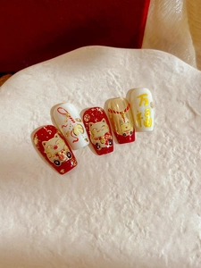 Macro detail of red and gold Maneki-neko nail art stickers on square-oval fake nails