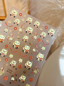 Macro view of gold-stamped Maneki-neko nail stickers with lucky charms and Chinese coins
