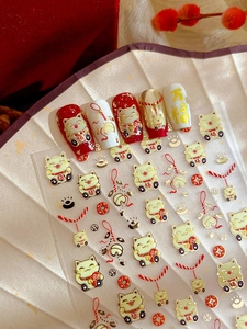 Close-up of Maneki Neko nail stickers with gold foil lucky charms and festive red accents