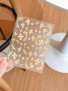 Dettaglio di adesivi nail art floreali con fiori dorati e foglie blu su un foglio unico