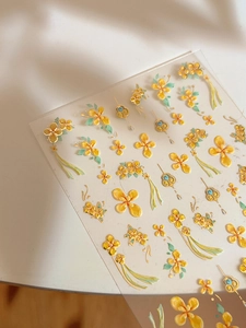 Vista macro di adesivi per unghie a rilievo con fiori gialli e bordi dorati