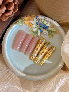 Detail of long pointed press-on nails with gold cloisonné patterns and pink finish