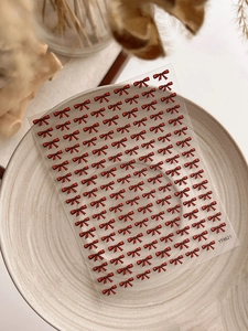 Macro shot of red ribbon bow 3D nail art stickers on a white ceramic plate