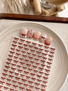 Detail of red bow nail stickers with heart and polka dot patterns on a ceramic tray