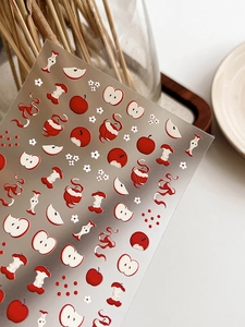 Détail de motifs de pommes rouges et stickers d'ongles fleurs blanches sur fini mat