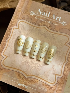 Detailed close-up of cream white long coffin nails with gold baroque floral patterns