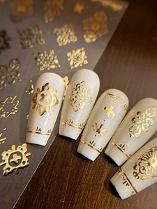 Detailed macro view of gold embossed bohemian nail stickers on white acrylic nails