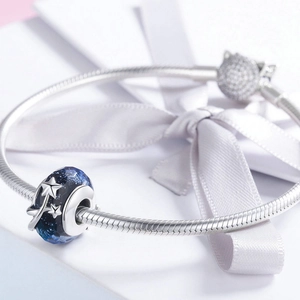 Makroaufnahme des silbernen Schlangenarmbands mit blauem Glasanhänger und Sternenmuster