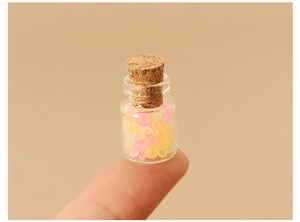 Miniature glass candy jar with cork stopper held on fingertip for dollhouse decor