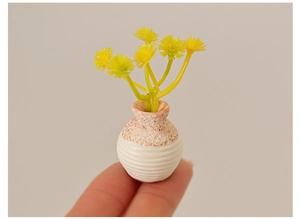 Detailed macro view of a miniature ceramic vase with yellow flowers held by a fingertip