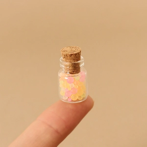 Miniature glass jar with cork stopper and colorful beads shown on fingertip scale