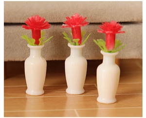 Detailed view of three miniature dollhouse vases with red flowers on a wooden surface
