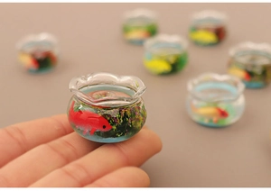 Detailed macro view of a miniature glass fishbowl with tiny red fish and green aquatic plants