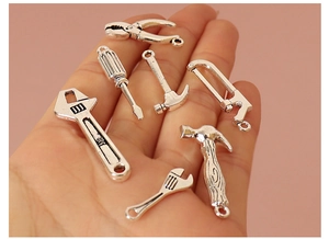 Miniature silver metal tool charms held in hand showing small scale for DIY dollhouse
