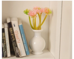 Miniature white dollhouse vase with pink daisy flowers placed on a clean bookshelf decor