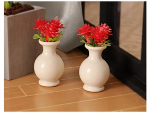 Miniature white ceramic dollhouse vases with red flowers on a wooden floor background