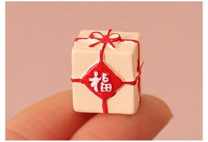 Miniature boîte cadeau beige avec nœud rouge et caractère Fu sur le doigt