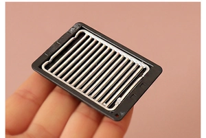Detailed close-up of a dollhouse miniature black barbecue grill with metal wire rack