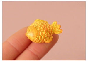 Macro shot of tiny orange miniature goldfish on a fingertip for dollhouse decor
