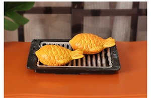 Macro detail of miniature Taiyaki models on a black rectangular grill for dollhouses