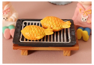 Detailed macro view of two resin taiyaki models on a miniature black barbecue grill