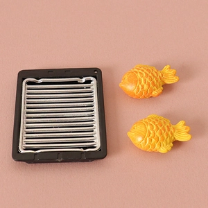 Miniature dollhouse BBQ grill with two tiny fish models on a textured pink surface