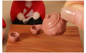 Macro detail of miniature teapot set with floral pattern held for scale comparison