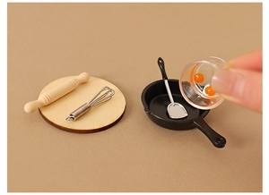 Miniature dollhouse kitchen set with whisk, rolling pin, and frying pan in hand
