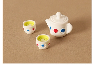Close-up of miniature dollhouse tea set with dotted teapot and yellow tea cups