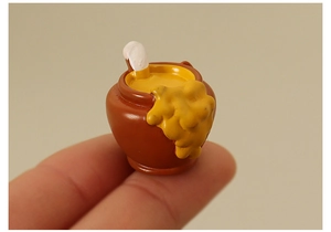 Dettaglio macro di un vasetto di miele in miniatura tenuto su un dito per scala di misura