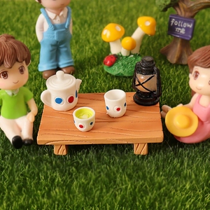 Miniature dollhouse picnic set with tiny tea set, lantern, and wooden table on green grass