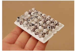 Miniature dollhouse quail eggs in white tray held by fingers showing realistic tiny scale