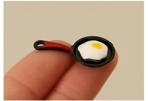 Miniature dollhouse frying pan with egg shown on a fingertip for size scale