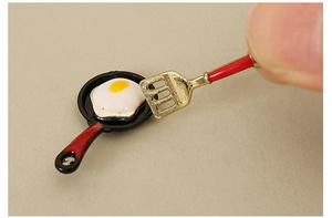 Close-up of miniature dollhouse frying pan set with tiny egg and gold spatula