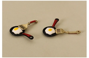 Detailed close-up of a dollhouse miniature frying pan and gold spatula pendant set