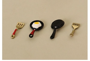 Detailed view of dollhouse miniature frying pans and golden spatulas with tiny fried eggs