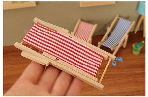 Detailed close-up of a miniature dollhouse folding beach chair with red striped canvas