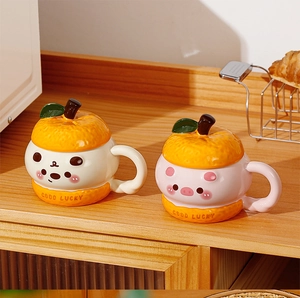 Two creative ceramic mugs with orange-style lids on a wooden desk with croissants