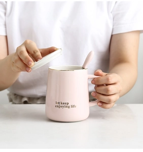 Pink ceramic mug set with gold text and lid held against a marble tabletop background