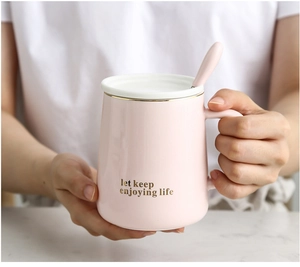 Detail of pink ceramic mug with gold rim, lid, spoon, and keep enjoying life lettering