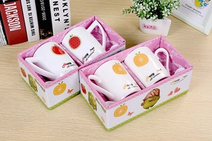 Detailed view of ceramic fruit-themed mugs in pink cartoon gift boxes on a wooden table