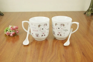 Detail of white ceramic mug with pink cartoon bear prints and matching spoons on wood