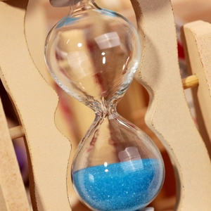 Creative wooden hourglass with blue sand and wave-shaped natural wood frame on a desk