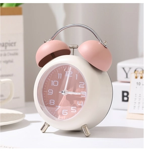 Gros plan d'un réveil à double cloche avec cadran rose et cadre en métal crème