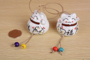 Close-up of ceramic lucky cat bells with colorful beads on a light wood background