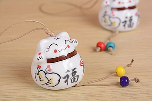 Macro detail of Maneki Neko ceramic bell with hand-painted plum blossoms and beads