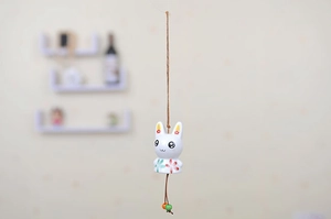 Detail of white ceramic rabbit wind chime with floral patterns and woven hanging rope