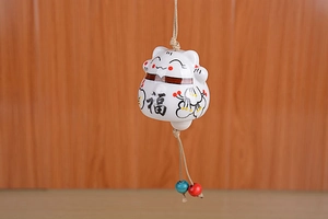 Close-up of Japanese ceramic fortune cat wind chime with lucky Fu character and floral detail