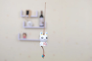 Detail of a white ceramic bunny wind chime with floral patterns and a brown hanging cord